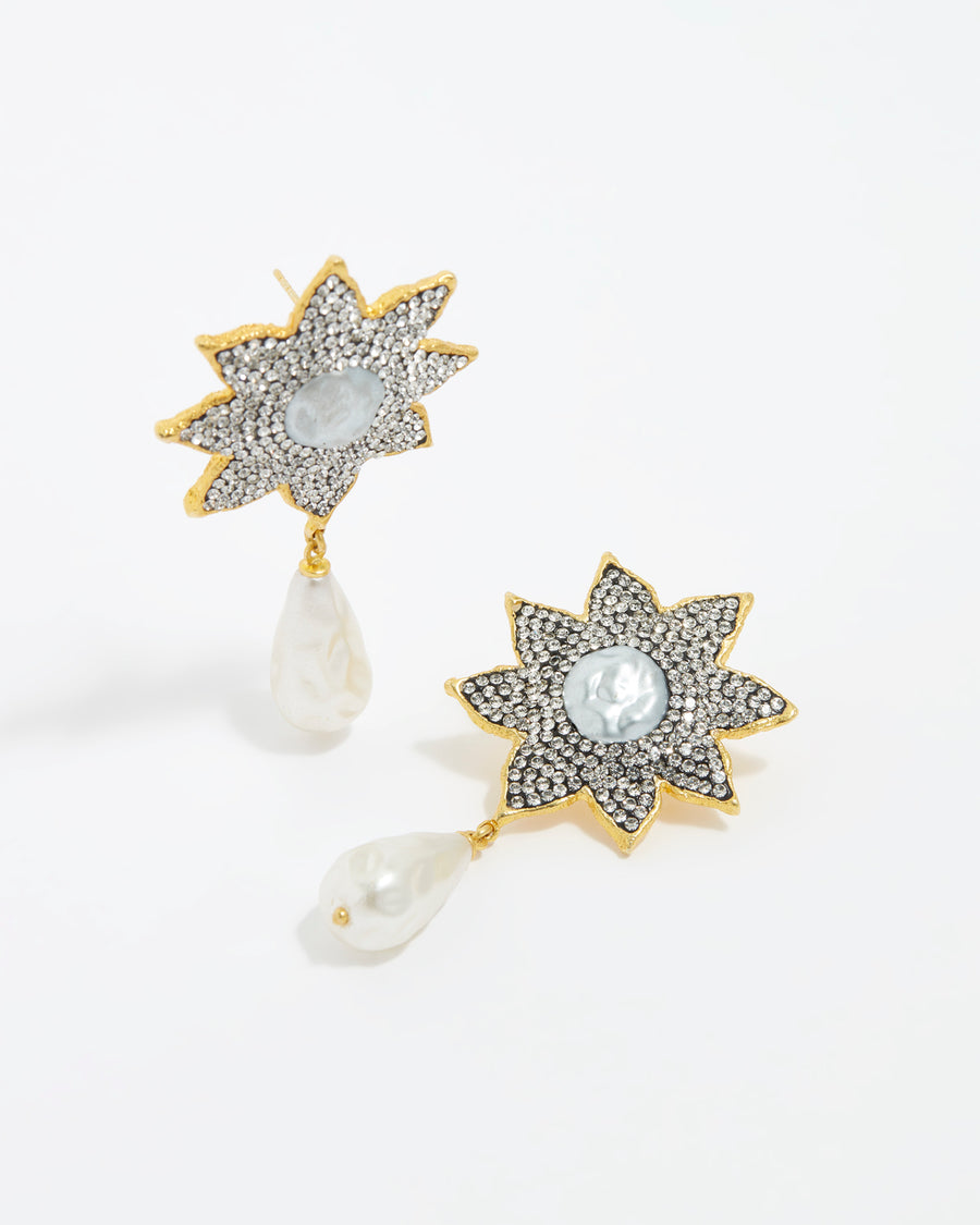 close up image shot of large clear crystal embellished flower shaped earrings featuring a round baroque pearl centre and large hanging baroque pearls on a white back ground