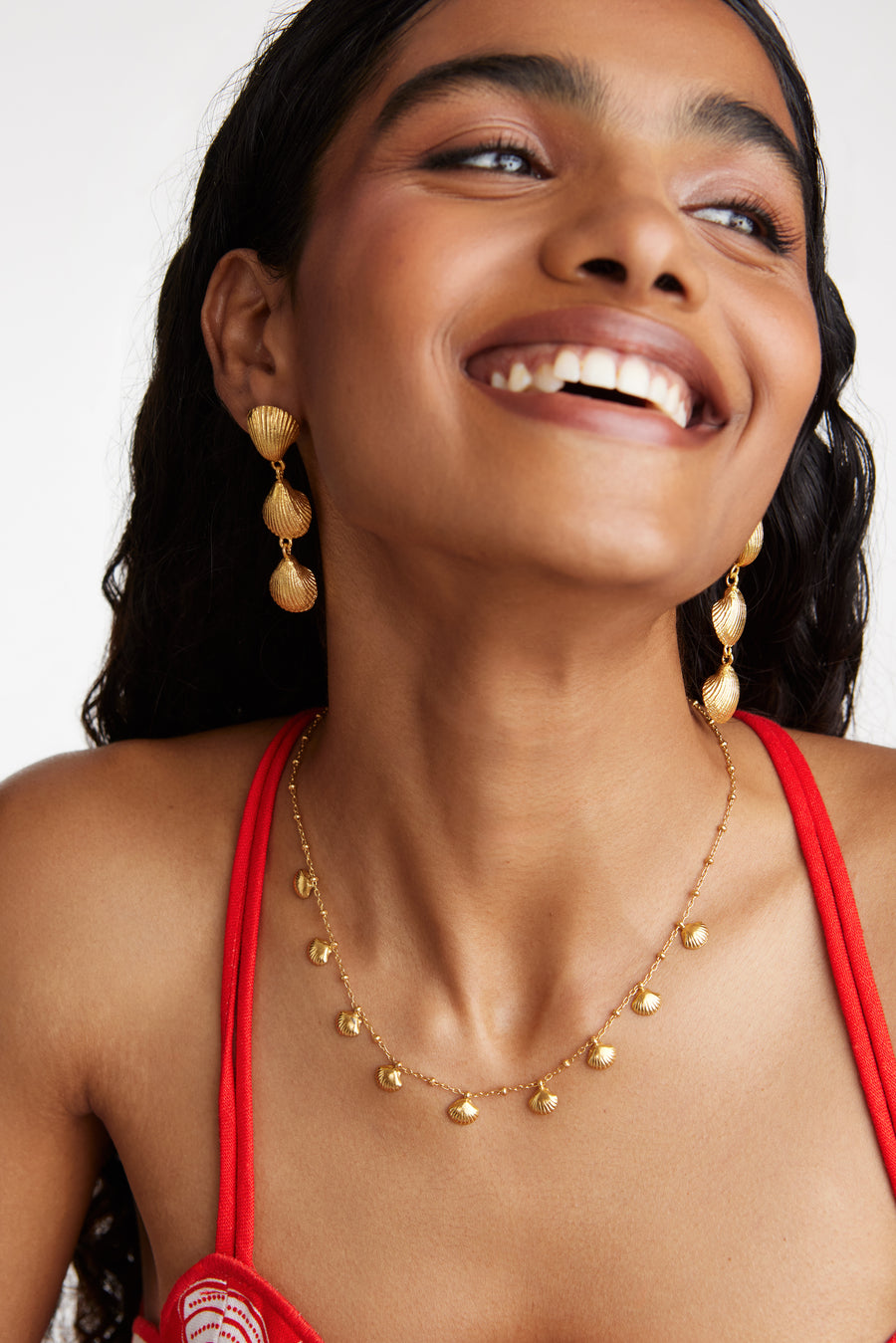 Smiling Model shot wearing the Soru Jewellery gold shell drop earrings with a mini shell necklace