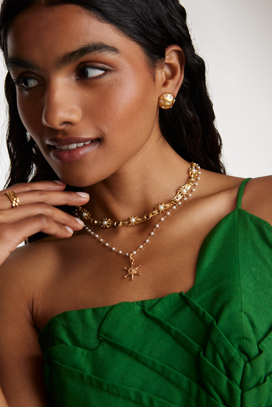 close up model shot of round gold star etched earrings with clear crystal embellishment while model is smiling. Model also wearing a gold chunky white bead emellished necklace and a delicate pearl beaded necklace with a ships wheel charm 